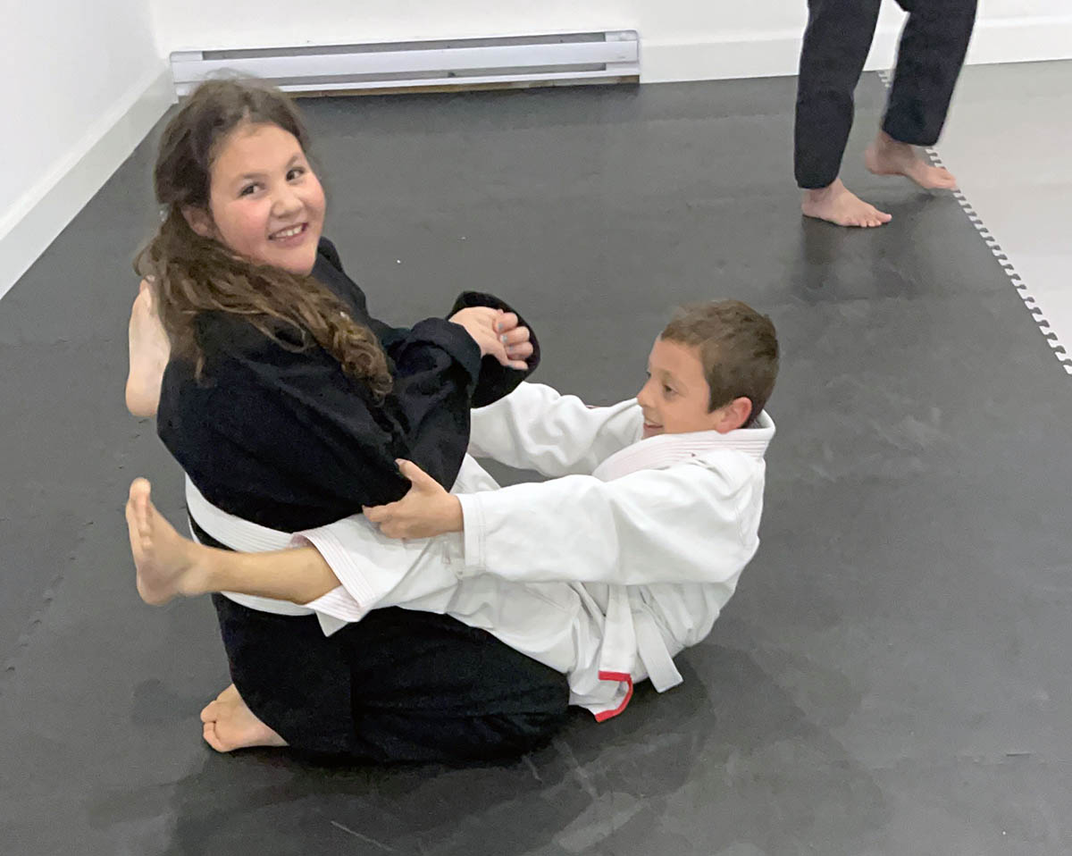 bjj-image-3 Young Girl assisting a younger student during a Brazilian Jiu-Jitsu class.