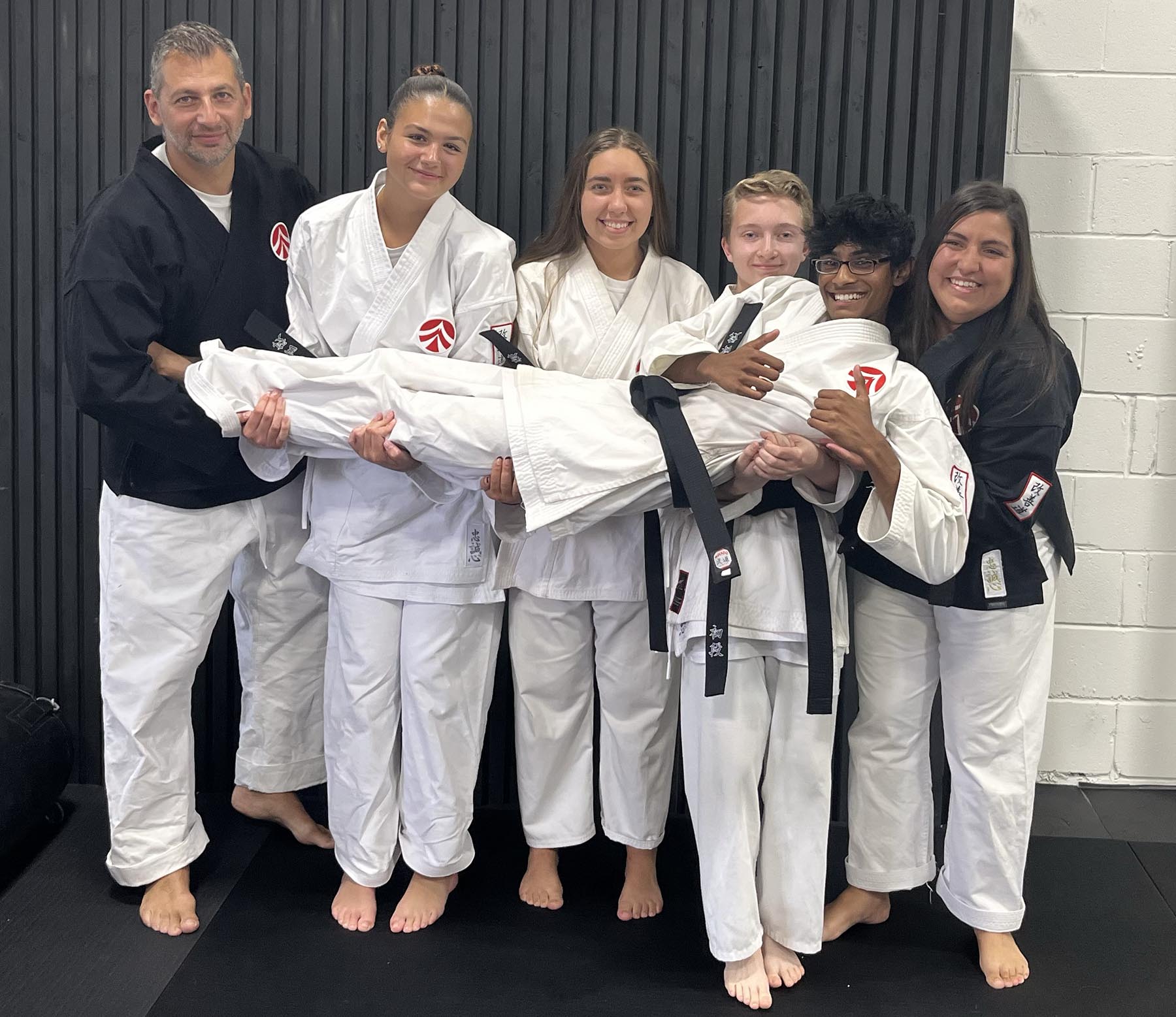 academy-of-martial-arts-missisauga-team Image of karate students and instructors in their uniform holding a student horizontally in front of them posing for a fun photo.