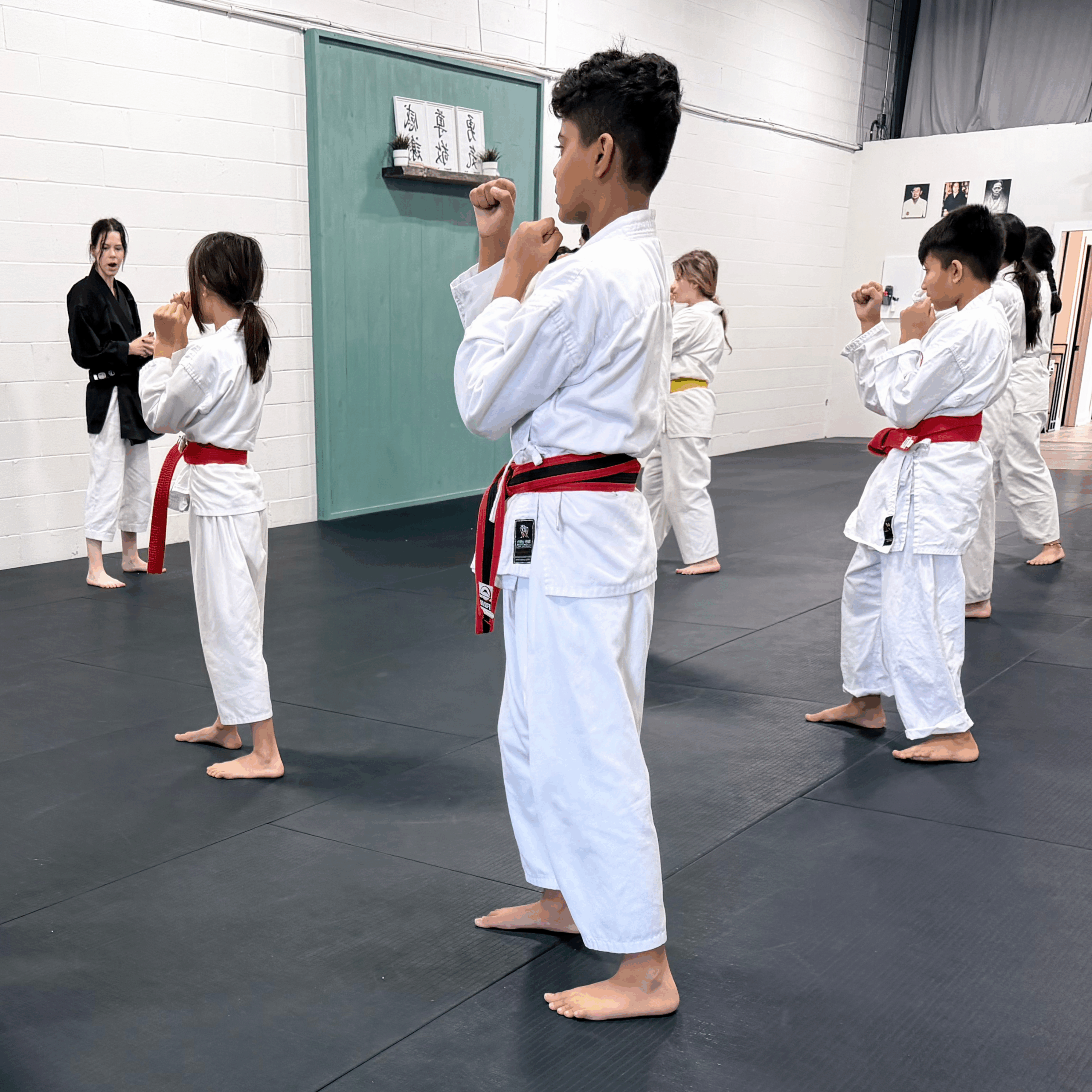 3 Karate students lined up and practicing their kata under supervision.